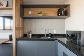 A modern kitchen with a built-in microwave, kettle, and coffee machine on the countertop. - Studio Moderno com Vista e Lazer Completo (Porto Alegre)