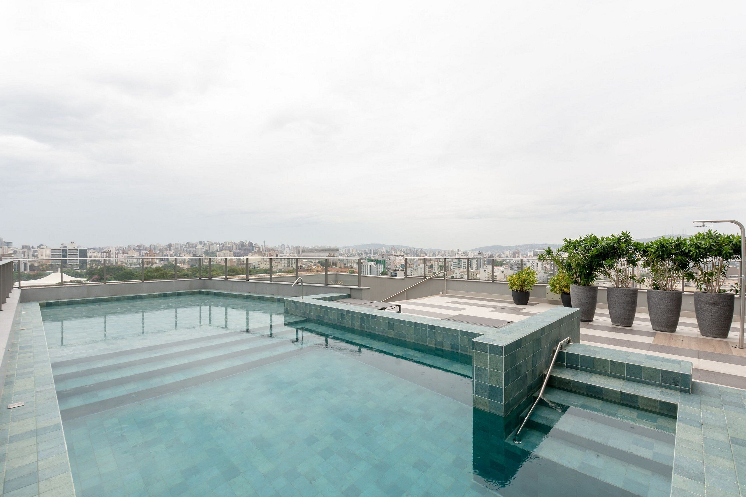 Piscina no terraço com vista para a cidade, rodeada por plantas em vasos.