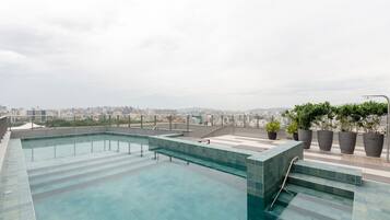 Piscina no terraço com vista para a cidade, rodeada por plantas em vasos.