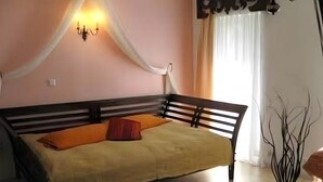 Un dormitorio con cama, mesita de noche, luz de pared y ventana con cortinas.