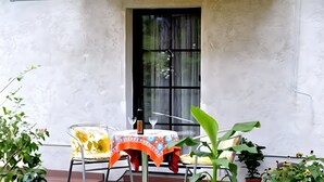 Eine Terrasse mit Tisch, Stühlen, einem Fenster und Kübelpflanzen.