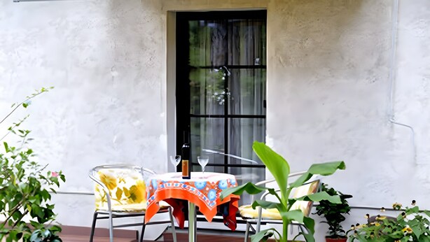 Un patio con una mesa, sillas, una ventana y plantas en macetas.