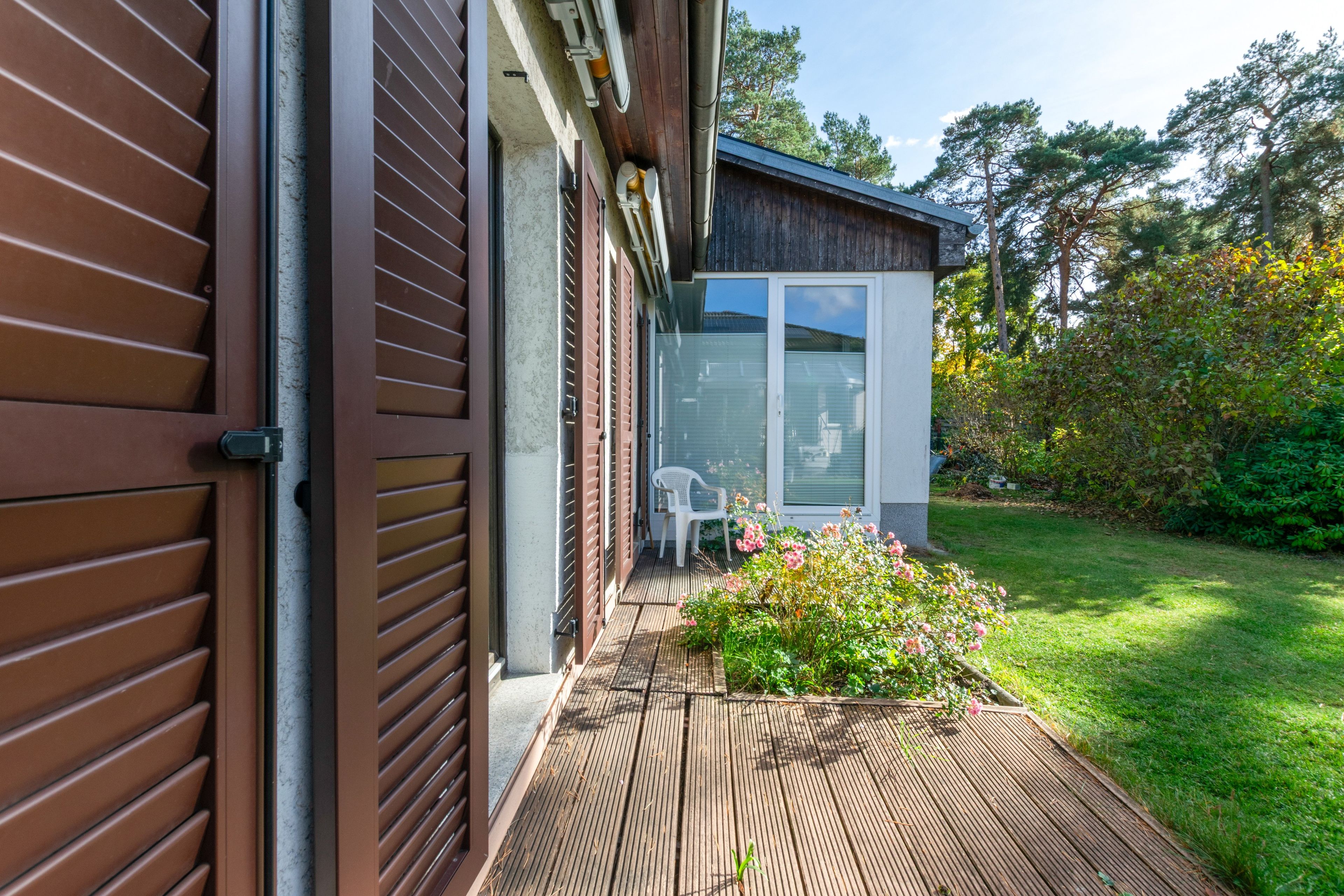 A modern house with a wooden deck, a glass door, and a garden with flowers.