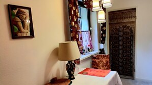 Una habitación con una mesa, una lámpara, un espejo decorativo, una cortina estampada y una puerta con diseño intrincado.