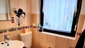 Un baño con lavamanos, inodoro y ventana con cortinas.