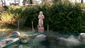 A statue in a garden with a mesh fence and rocks. - Apartment "La Vida" for 3 Guests, 60 m² with Shared Garden, Wi-Fi and Air Conditioning (Hoppegarten)