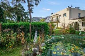 A residential area with a house, a fenced garden, and a pond with lily pads. - Apartment "La Vida" for 3 Guests, 60 m² with Shared Garden, Wi-Fi and Air Conditioning (Hoppegarten)