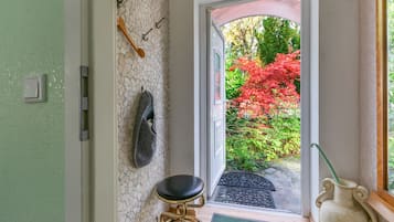 A room with a stone wall, a black leather stool, a white vase, and a view of a garden with red foliage.