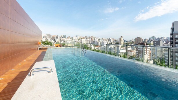 A rooftop infinity pool with a city view, a wooden deck, and a glass railing. - Studio Moderno e Conectado em Porto Alegre (Porto Alegre)