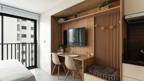 A modern kitchen with a built-in TV, wooden cabinetry, and a dining area with two chairs. - Studio Moderno | Lazer Completo em Porto Alegre (Porto Alegre)
