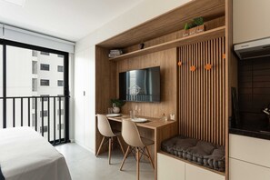 A modern kitchen with a built-in TV, wooden cabinetry, and a dining area with two chairs. - Studio Moderno | Lazer Completo em Porto Alegre (Porto Alegre)