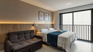 A bedroom with a bed, a sofa, and a large window. - Studio Moderno | Lazer Completo em Porto Alegre (Porto Alegre)