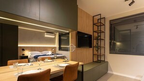 Una habitació d'hotel moderna amb zona de menjador, llit, televisió i una finestra gran.