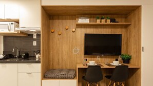 A compact kitchen with a built-in TV, wooden accents, and a small dining area with two chairs. - Studio moderno: rooftop no coração do Rio Branco (Porto Alegre)