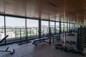 Uma academia com grandes janelas, equipamentos de musculação e vista para a cidade.