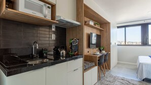 A modern kitchen with a microwave, kettle, and sink; a dining area with a TV and a small table; and a bedroom with a bed and a view. - Studio moderno: rooftop no coração do Rio Branco (Porto Alegre)