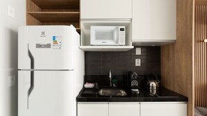 A kitchen with a white refrigerator, a microwave, a kettle, and a sink. - Studio sofisticado e moderno no bairro Rio Branco (Porto Alegre)
