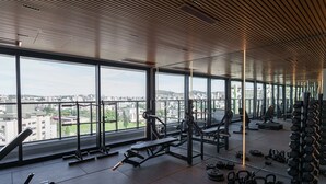 Uma academia com grandes janelas, equipamentos de musculação e vista para a cidade.
