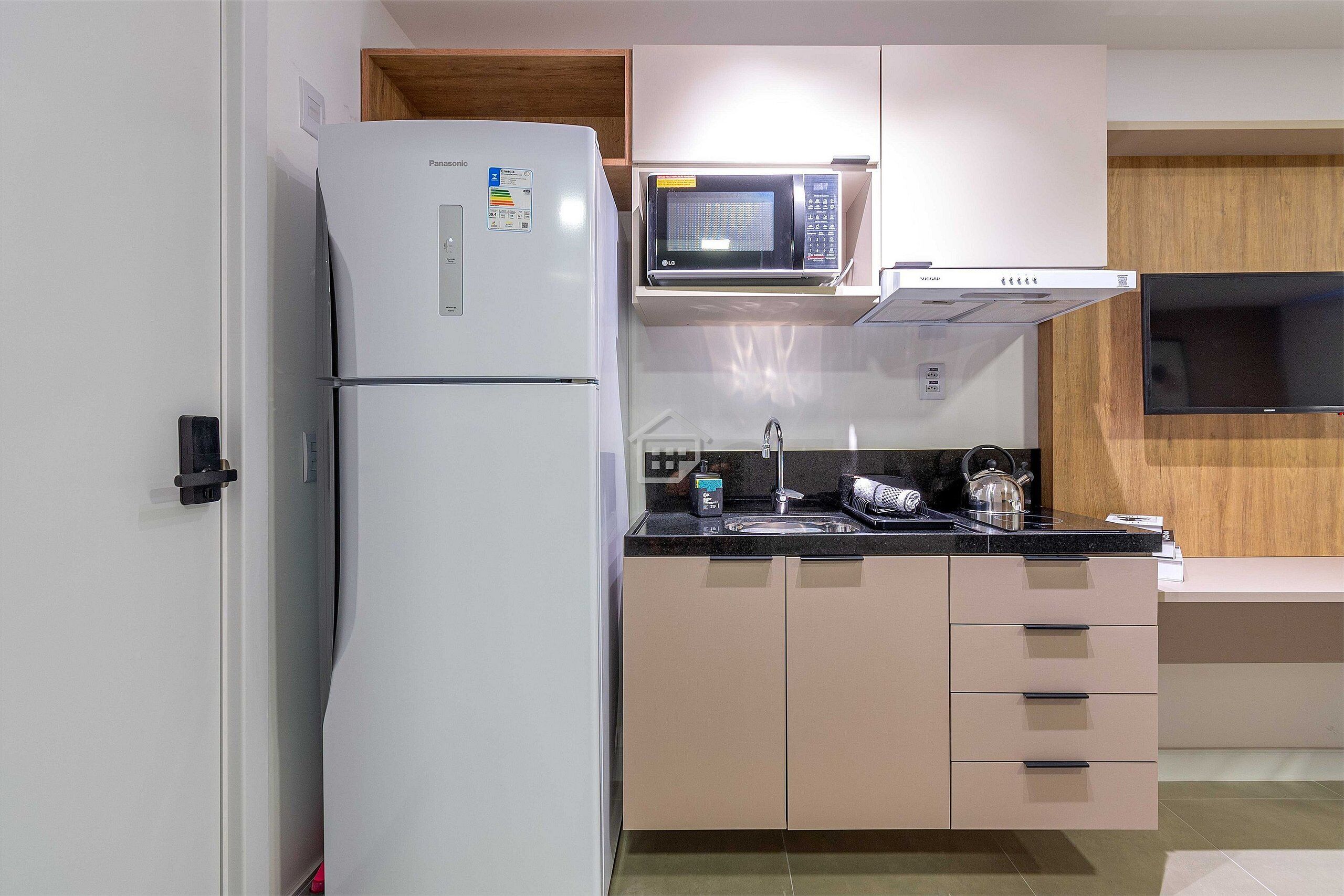 Una cucina compatta con frigorifero, microonde e piano cottura, caratterizzata da un design minimalista e dettagli in legno.