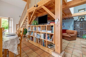 A wooden interior with a dining area, bookshelves, a television, and a leather sofa. - Rural Gîte des Loubatous with Mountain View and Wi-Fi (Castelnaudary)