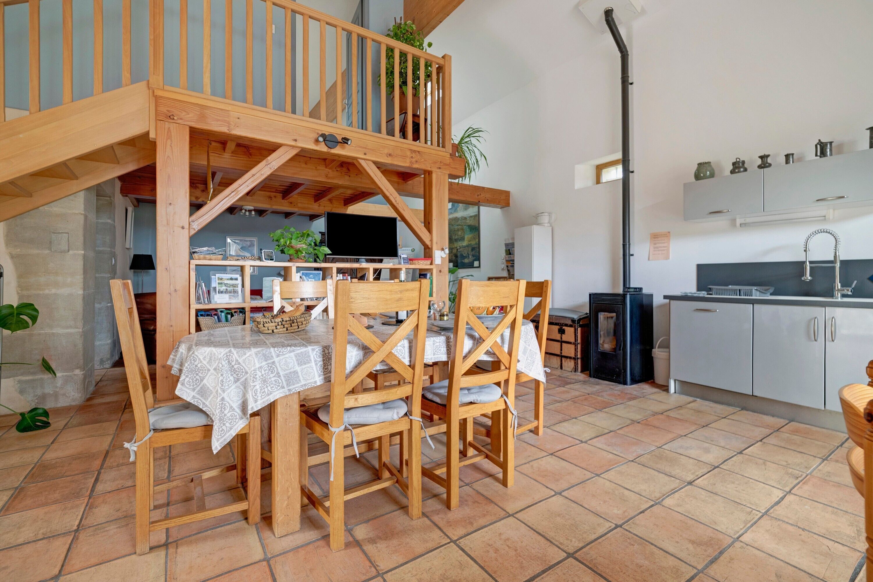 A dining area with a wooden table and chairs, a kitchen with white cabinets, and a balcony with wooden railings.