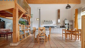 Ein geräumiger Wohnbereich mit einer Holztreppe, einem Esstisch mit Stühlen, einer Küchenzeile und einem Bücherregal.