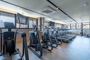 Ein Fitnessstudio mit mehreren Laufbändern, Ergometer und einem großen Fenster mit Blick auf die Stadt.