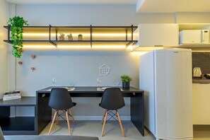 Eine moderne Küche mit schwarzem Arbeitsplatz, zwei schwarzen Stühlen, einem weißen Kühlschrank und einem Regal mit Pflanzen.