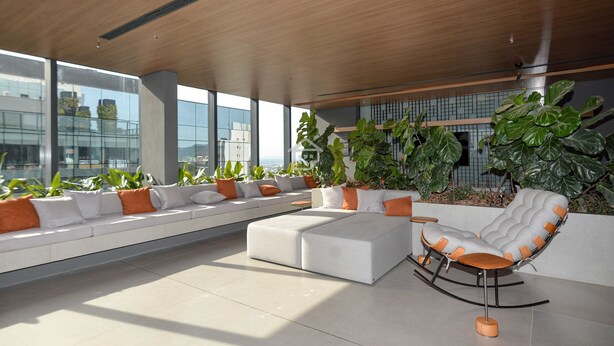 Un área de descanso moderna con un sofá blanco, un sillón mecedor y plantas grandes en macetas.