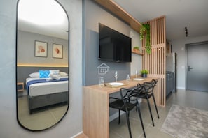 Ein modernes Zimmer mit einem Bett, einem Esstisch mit Stühlen, einem darüber montierten Fernseher und einem Kühlschrank in der Ecke.