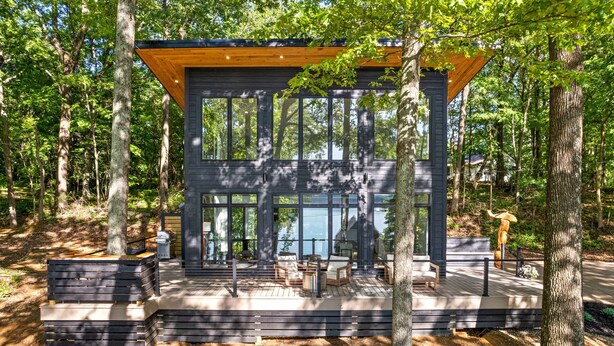 A modern cabin with large windows, a deck, and outdoor seating.