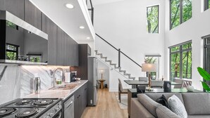 A modern kitchen with a central island, a dining area with a table and chairs, a staircase, and a living room with a sofa.