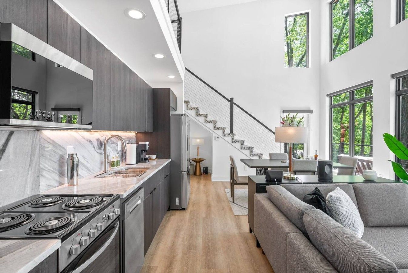 Une cuisine moderne avec un îlot central, un coin repas avec un escalier, et un salon avec un canapé.