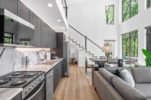 A modern kitchen with a central island, a dining area with a staircase, and a living room with a sofa.