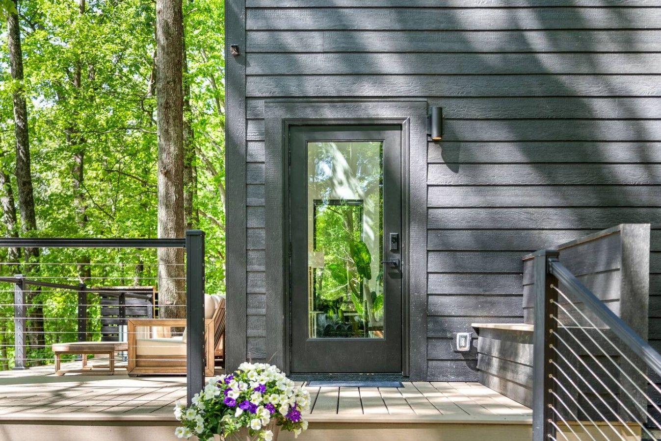 A modern house with a dark grey exterior, a front door, and a small porch area with a bench and a flower arrangement.