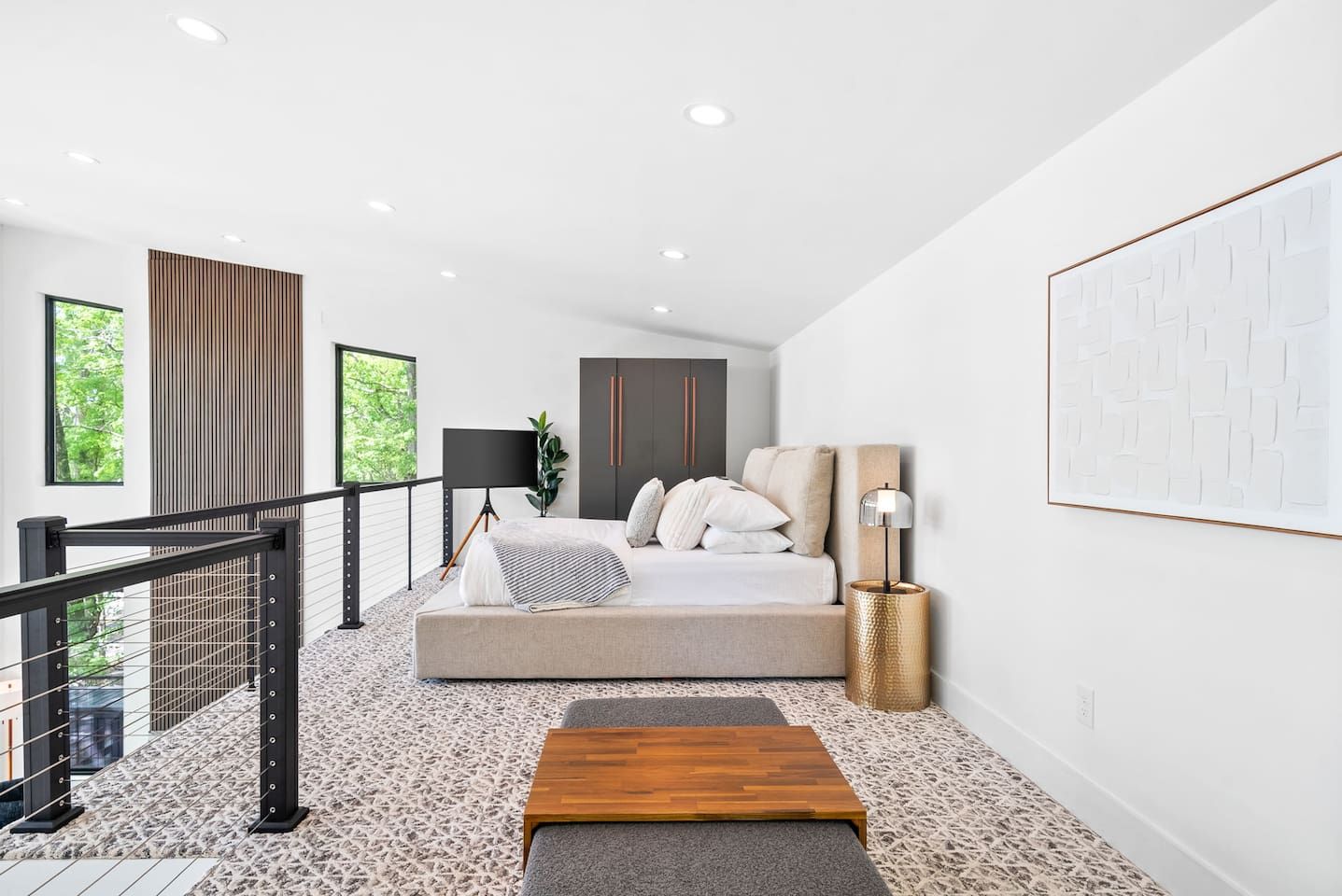 A modern bedroom with a bed, a bedside table, a lamp, and a view of greenery outside.