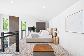 A modern bedroom with a bed, a bedside table, a lamp, and a view of greenery outside.