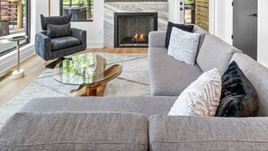 A spacious living area with a fireplace, large windows, and a high ceiling.