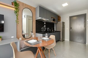 Une cuisine moderne avec des meubles gris, un réfrigérateur en acier inoxydable et un coin repas comprenant une table ronde et des chaises.