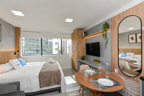 Une chambre d’hôtel moderne équipée d’un lit, d’une table à manger avec des verres, d’une télévision et d’un grand miroir.