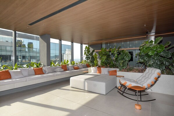 Un espace de détente moderne avec un canapé blanc, un fauteuil à bascule et de grandes plantes en pot.