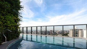 Une piscine à débordement située sur le toit, offrant une vue sur la ville et entourée de verdure.
