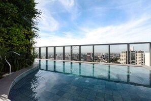 Une piscine à débordement située sur le toit, offrant une vue sur la ville et entourée de verdure.