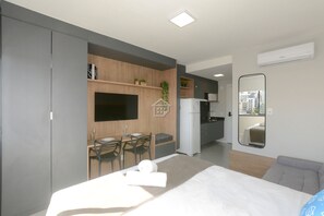 Habitación de hotel moderna con cama, escritorio con silla, kitchenette pequeña y espejo grande.