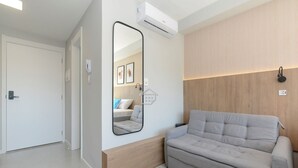 A modern room with a sofa, a mirror, an air conditioner, and a wooden accent wall. - O Seu refúgio de estilo no coração do Moinhos (Porto Alegre)