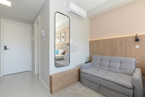 Quarto moderno com sofá, espelho, ar-condicionado e uma parede de destaque em madeira.