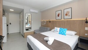 A hotel room with a bed, a desk, a chair, a mirror, and a wardrobe. - Apto Aconchegante Próximo ao Parque Moinhos (Porto Alegre)