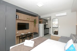 Una moderna camera d'albergo con un letto, una scrivania, una sedia, una TV a schermo piatto, un angolo cottura e uno specchio.