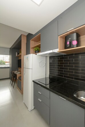 Uma cozinha moderna com geladeira, painel de azulejos pretos e janela com vista para a paisagem urbana.