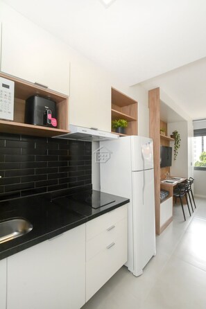 A modern kitchen with white cabinets, a black countertop, and a white refrigerator. - Apartamento Elegante ao Lado do Parque Moinhos (Porto Alegre)